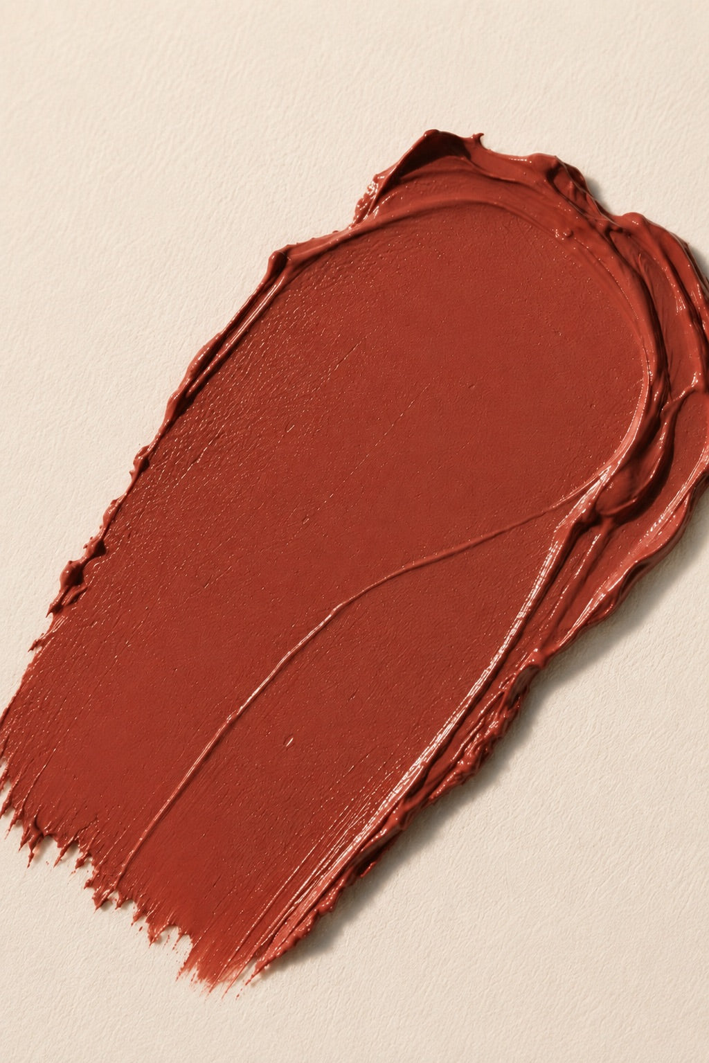 A textured swipe of warm terracotta or rust-brown cream product, cream makeup, on a light beige background.