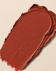 A textured swipe of warm terracotta or rust-brown cream product, cream makeup, on a light beige background.